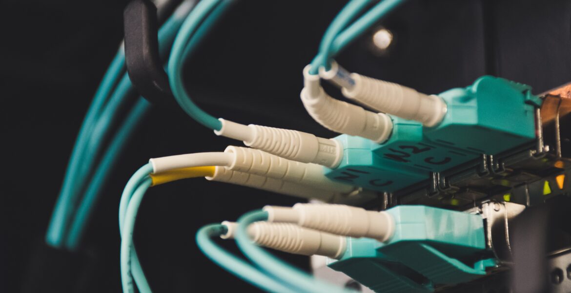 Primer plano de cables Ethernet verde azulado enchufados en un panel de conexiones de red en un bastidor de servidores, tenuemente iluminado.